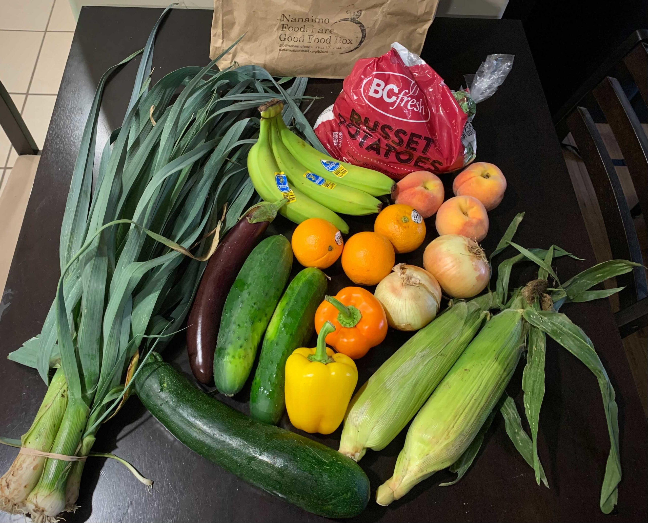 contents of the Good Food box, it consists of green onions, corn, oranges, peppers, zucchinii, onions, bananas, and potatoes.